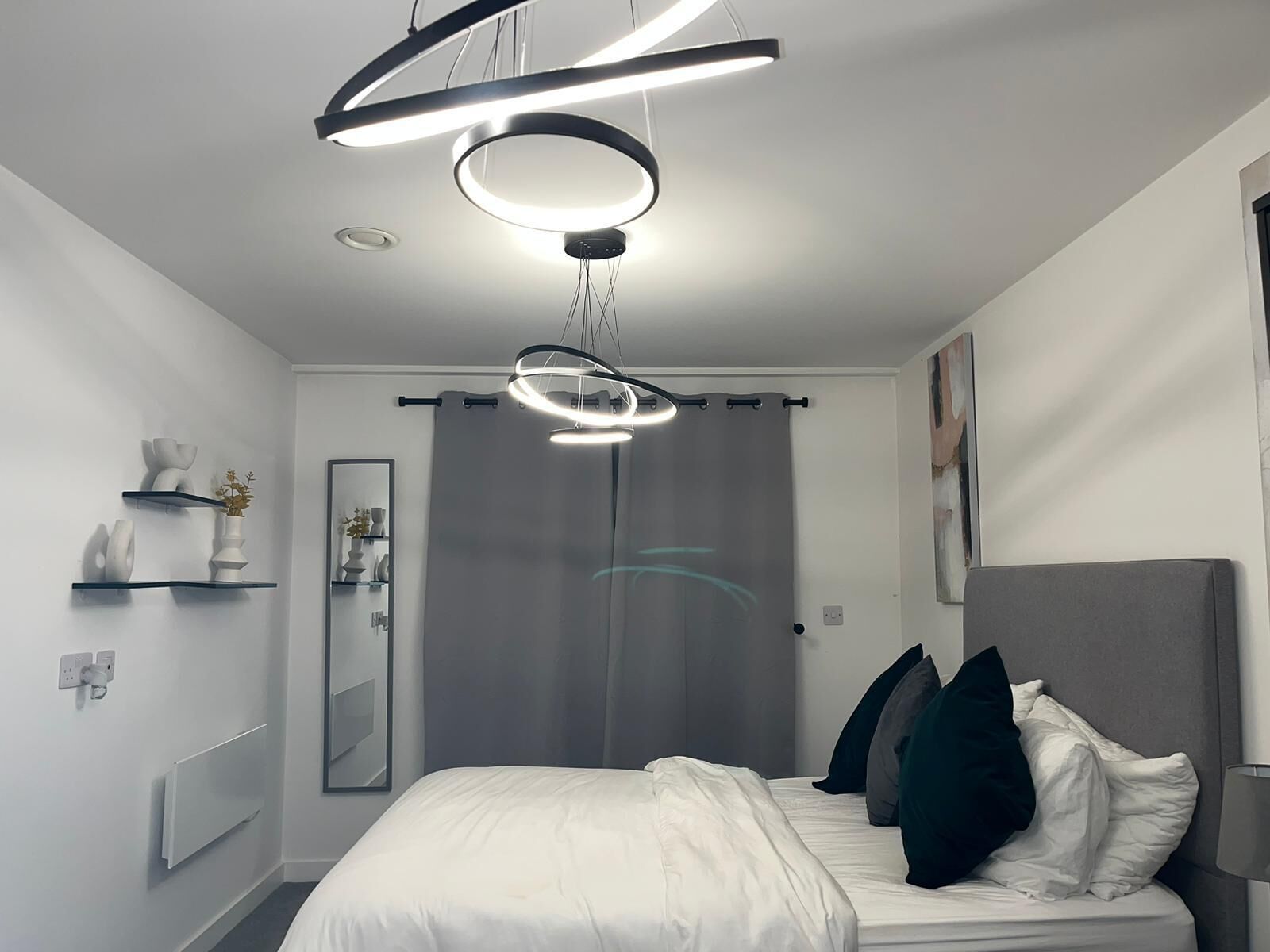 Une chambre moderne avec un lit, des tables de chevet, un miroir et un luminaire au plafond.
