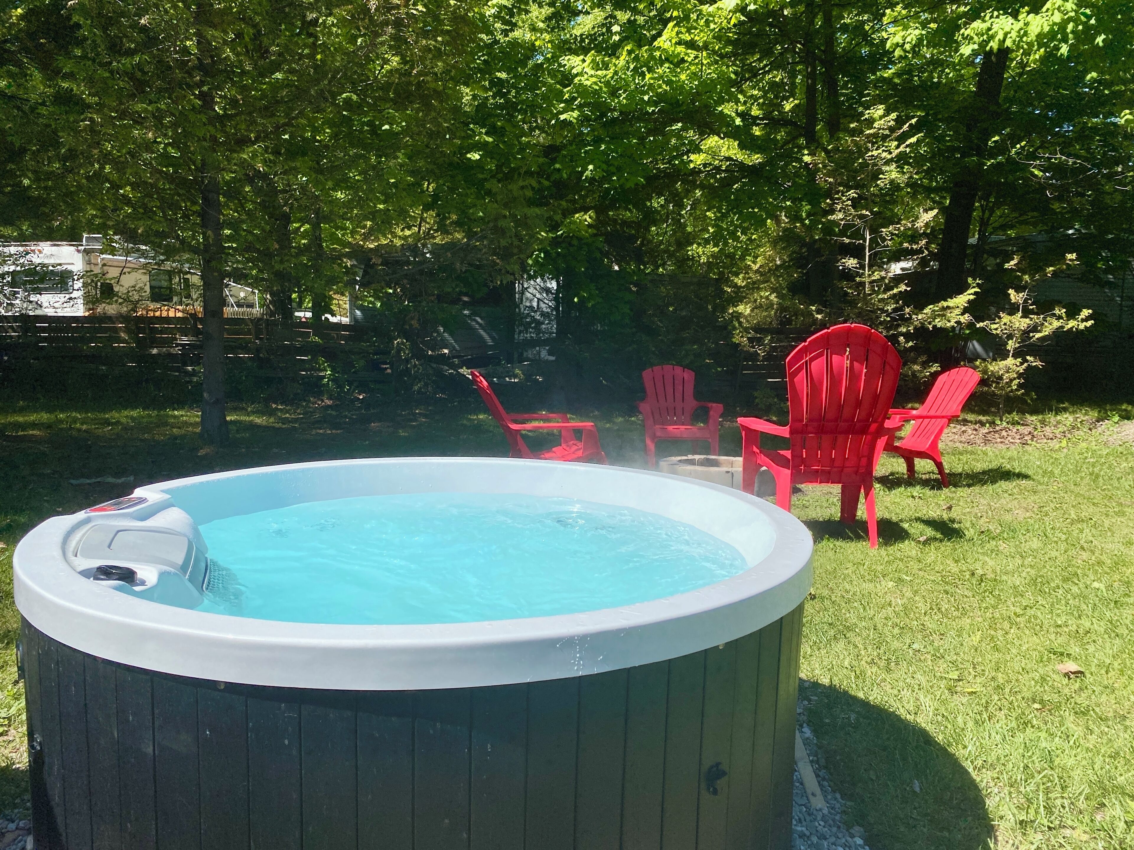 A hot tub surrounded by red chairs in a grassy backyard with trees.