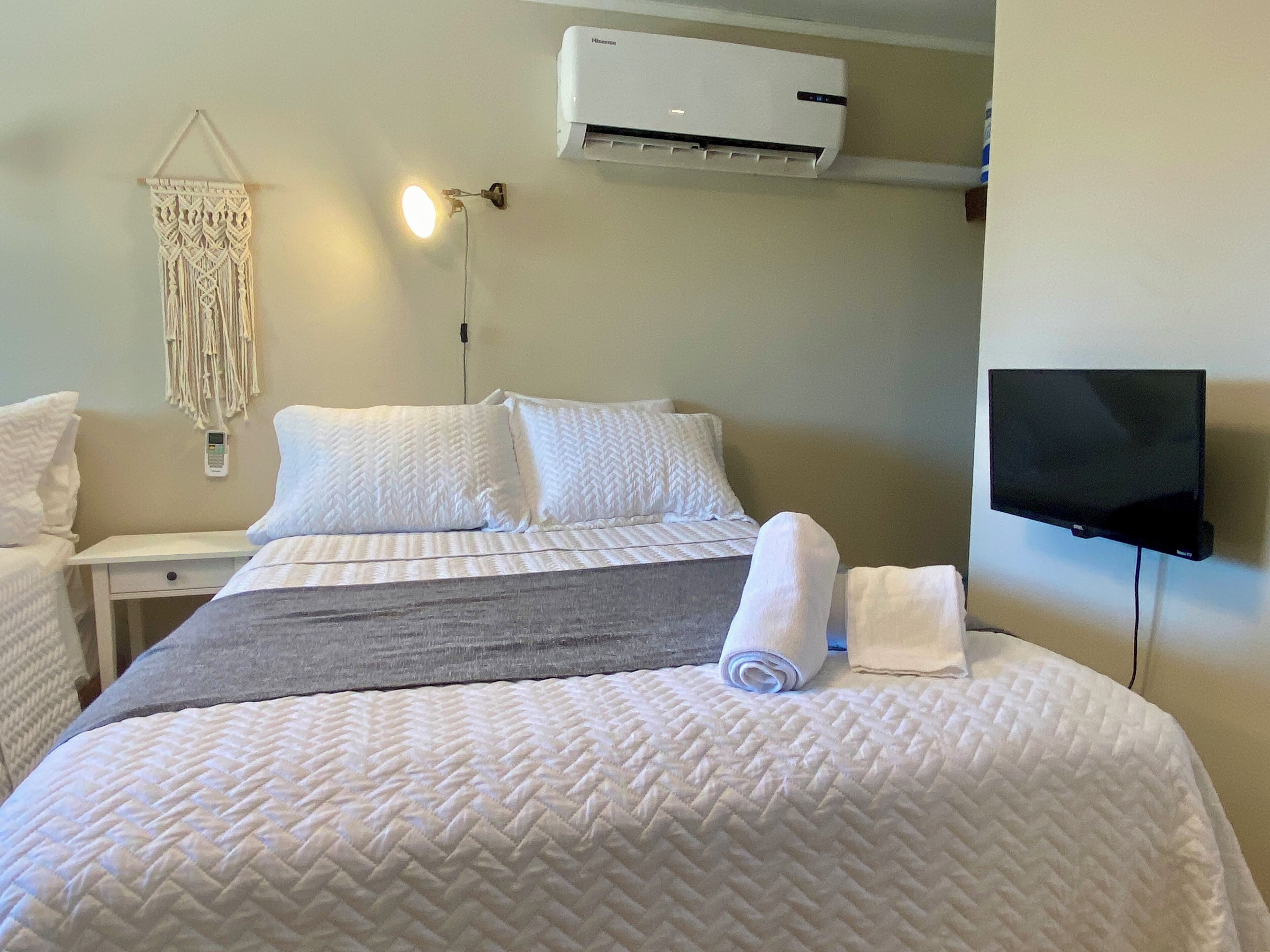 A hotel room with a bed, a bedside table, a wall-mounted TV, and an air conditioner.