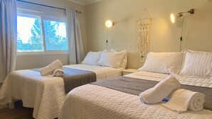 A hotel room with two beds, each with white bedding and a blanket. There is a window with curtains, a wall-mounted light, and a macrame wall hanging. - Cozy Bayfield Retreat • Pool & Hot Tub • 15min to Grand Bend • Lake Huron Nearby (Bayfield)
