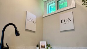 A kitchen with a stainless steel sink, a black faucet, and two framed signs on the wall reading "COFFEE" and "BON APPETIT". - Cozy Bayfield Retreat • Pool & Hot Tub • 15min to Grand Bend • Lake Huron Nearby (Bayfield)