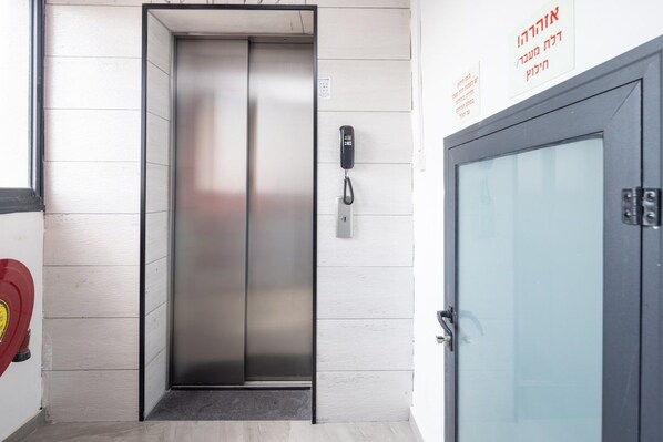 An elevator with a metallic finish, a wall-mounted phone, and a door with a glass panel.