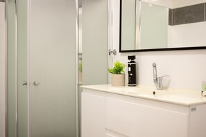A bathroom with a white countertop, a sink, a mirror, a potted plant, and a shower area. - Mamad Port Views Vista apartment (Haifa)