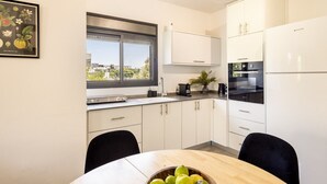A modern kitchen with white cabinets, a black countertop, a window with a view, and a table with a bowl of fruit.