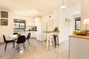 Une cuisine moderne avec des meubles blancs, un coin repas doté d’une table ronde et de chaises, et un bar avec des tabourets.
