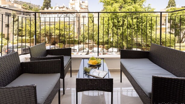A balcony with wicker furniture, a glass table, and a bowl of fruit.