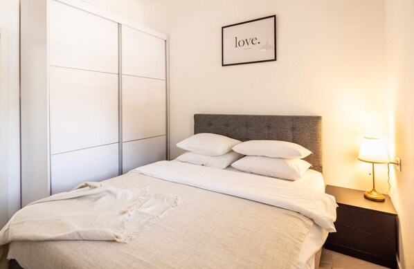 A neatly made bed with a grey headboard and white bedding, a bedside lamp, and a framed word 'love.'
