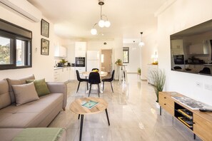 A modern living space with a sofa, dining area, kitchen, and a large window.