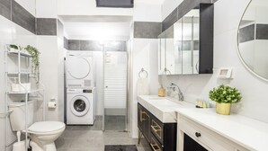 A compact bathroom with a toilet, washing machine, sink, and mirror. - Stylish 3BR City Stay Near Baháʼí Gardens (Haifa)