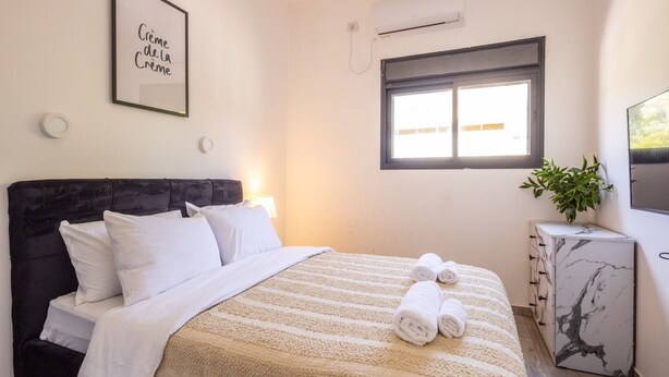 A hotel room with a bed, a nightstand, a TV, and a window. - Stylish 3BR City Stay Near Baháʼí Gardens (Haifa)