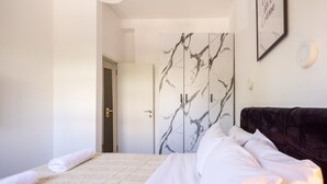 A bedroom with a bed, a dark headboard, a door with a marble design, and a framed quote on the wall. - Stylish 3BR City Stay Near Baháʼí Gardens (Haifa)