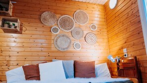 Een houten kamer met een bed, wanddecoraties van geweven materiaal en een klein plankje met planten.