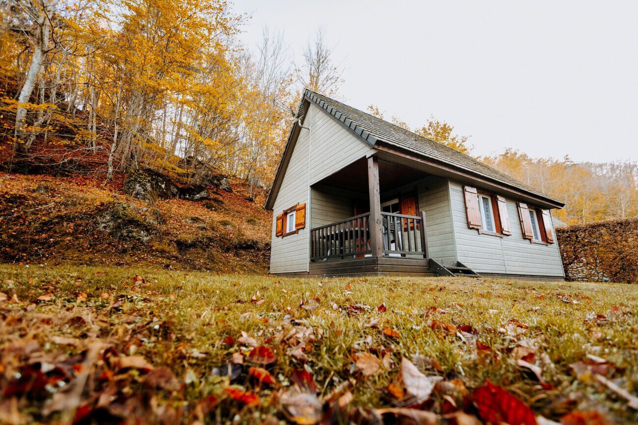 Een klein, gelijkvloers huisje met een veranda, omgeven door herfstkleuren.