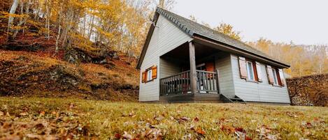 Een klein, gelijkvloers huisje met een veranda, omgeven door herfstkleuren.