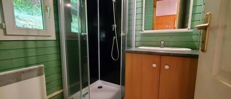 Un baño con ducha de vidrio, un lavamanos con espejo y una ventana con vista a la vegetación.