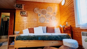 Ein Schlafzimmer einer Holzhütte mit einem Bett, Kissen und gewebten Wanddekorationen.
