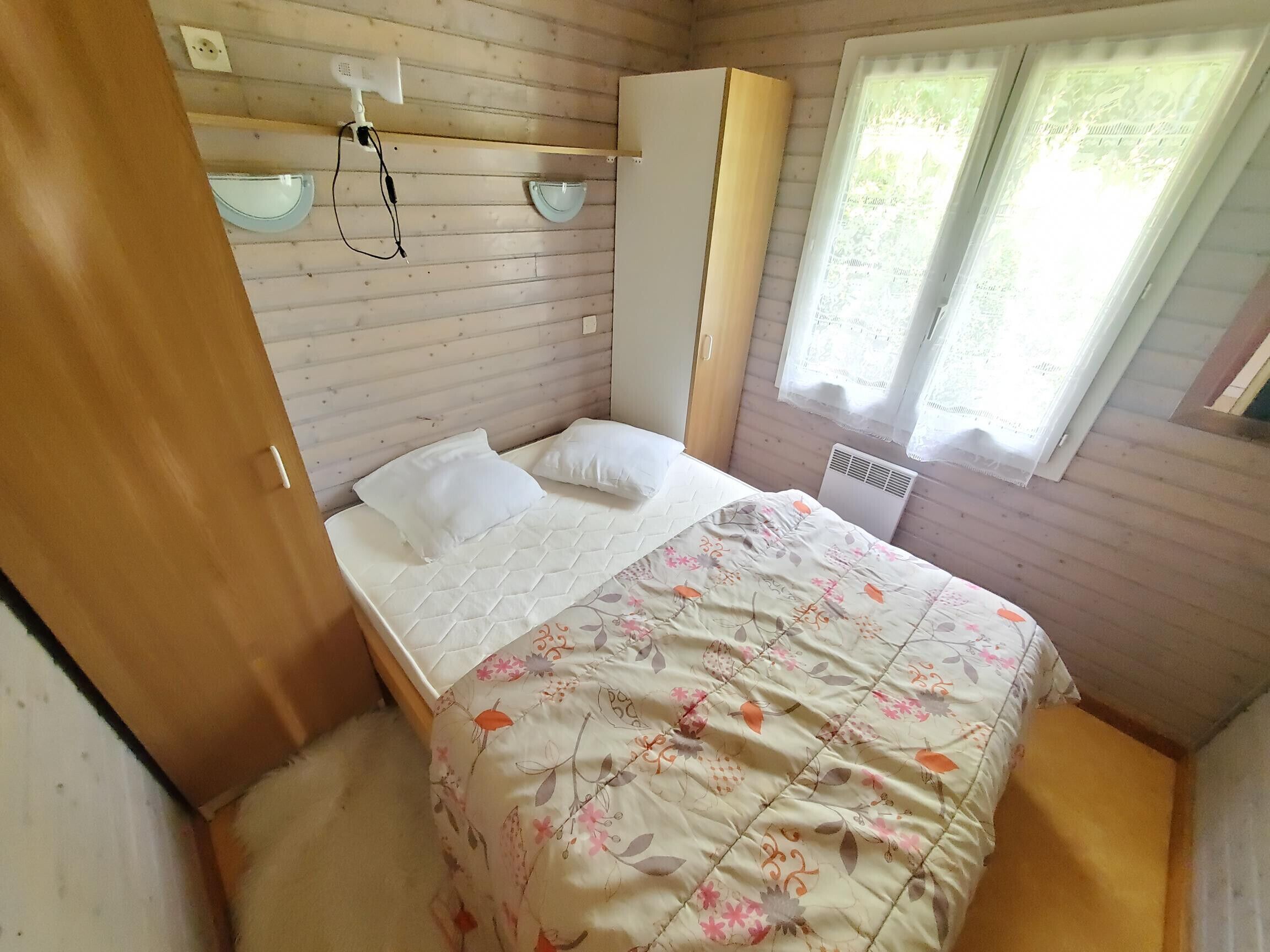 Un dormitorio pequeño y acogedor con cama, armario, calefactor y ventana con cortinas.