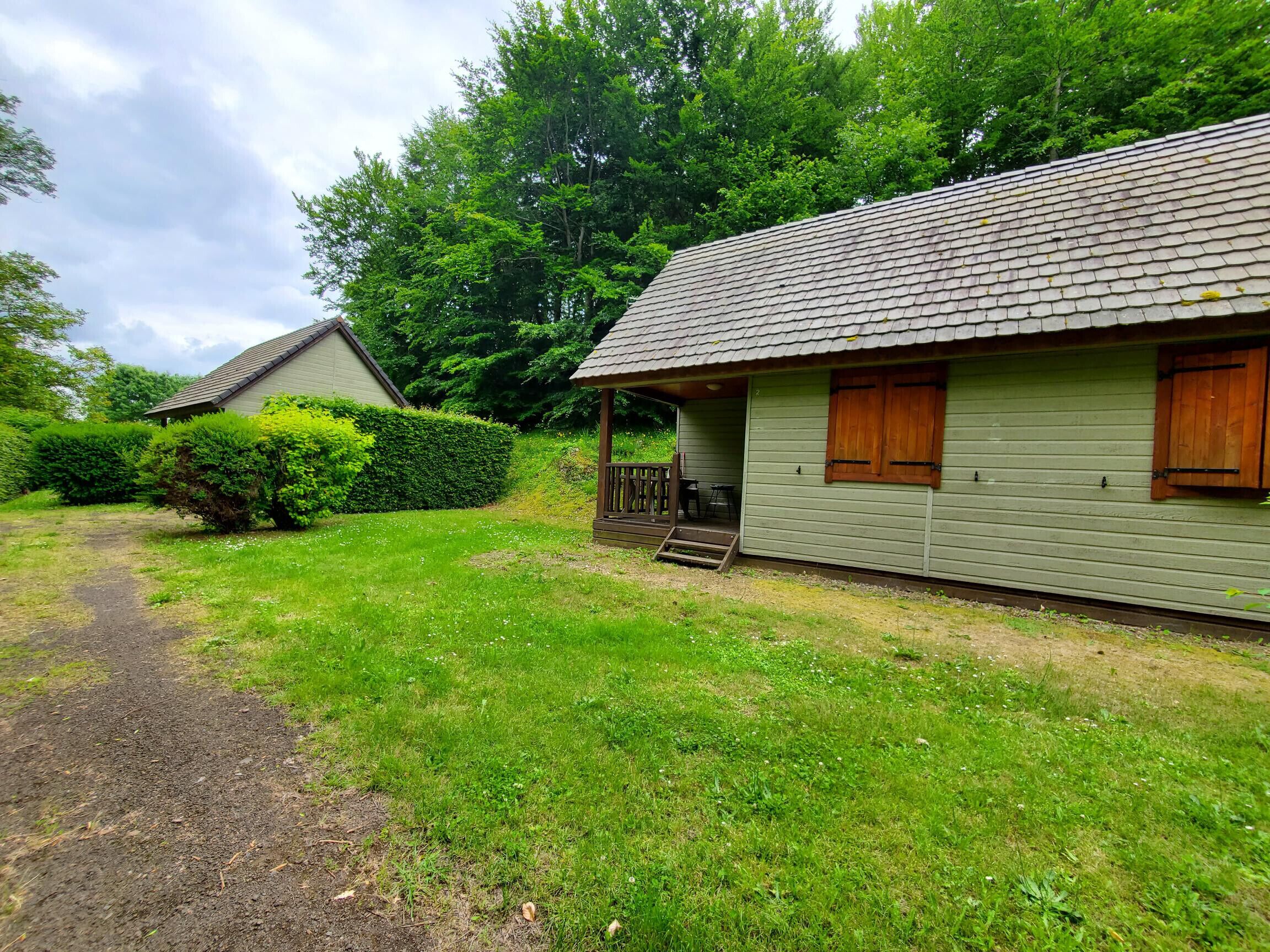 Un chalet de plain-pied doté d’un porche et d’une petite terrasse, entouré d’une végétation luxuriante et bordé d’un sentier menant à la maison.