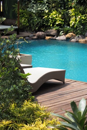 Zona de piscina con sillones de descanso y una terraza de madera.