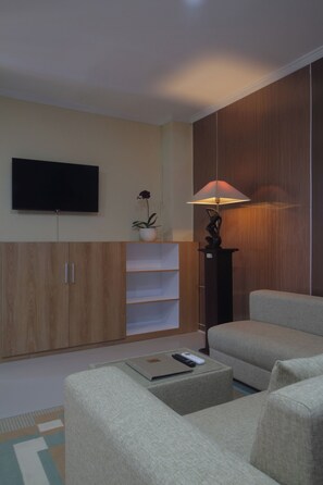 Ein modernes Wohnzimmer mit Flachbildfernseher, Sofa, Couchtisch, Lampe und einer Topfpflanze.