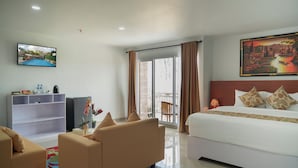 A hotel room with a bed, a sofa, a TV, a balcony with curtains, and a painting on the wall. - Parigata Resorts Jimbaran (Jimbaran)