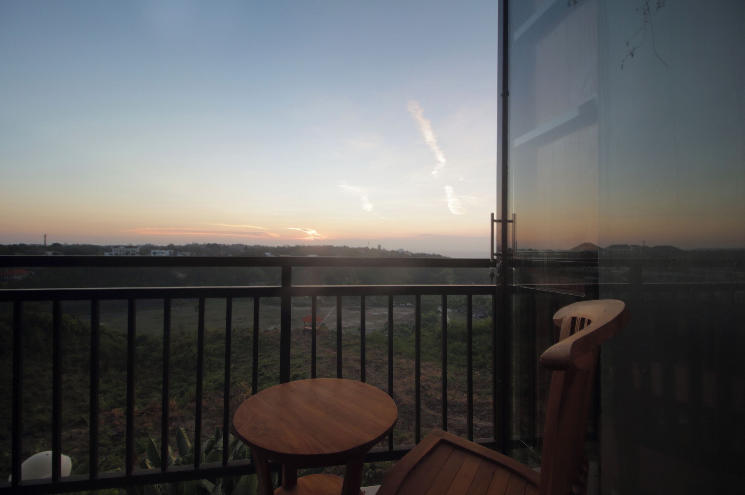 A balcony with a view of the horizon, a wooden table, and a chair.