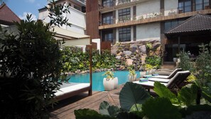 Area piscina con lettini, un molo in legno, piante e rocce varie.