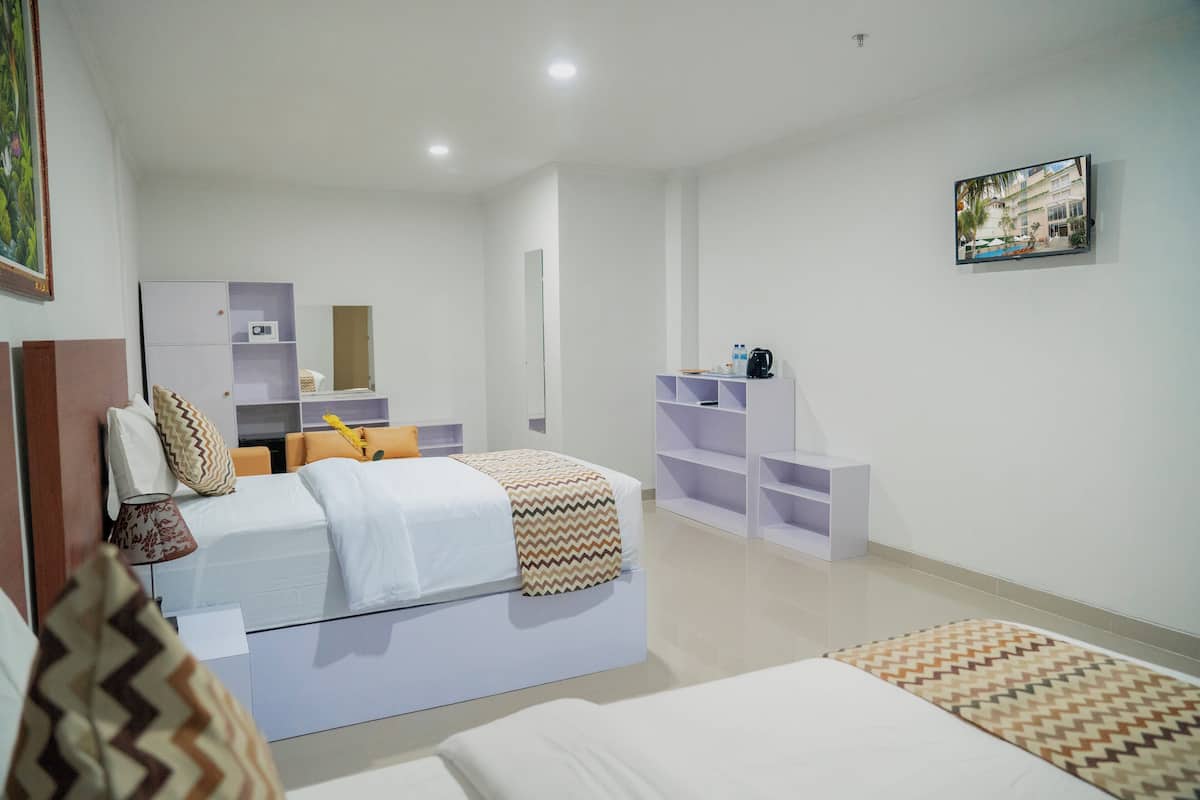 A modern hotel room with a large bed, a desk, and a chair. There is a small table with a water bottle and a cup. The room has white walls and a large window.