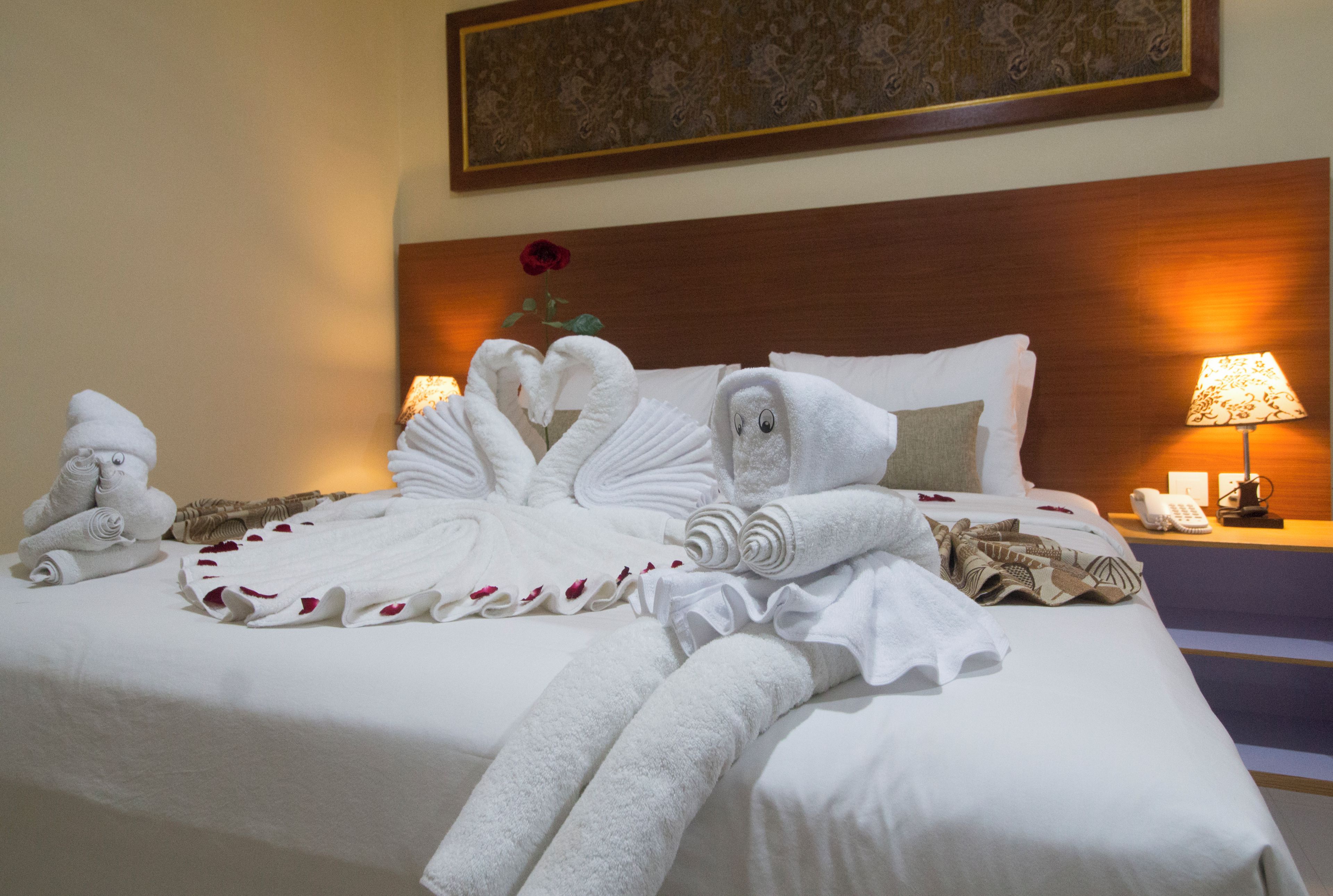 A hotel room with a neatly made bed, a bedside lamp, a telephone, and a painting on the wall.