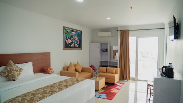 A hotel room with a bed, two sofas, a coffee table, a TV, and a window with curtains. - Parigata Resorts Jimbaran (Jimbaran)