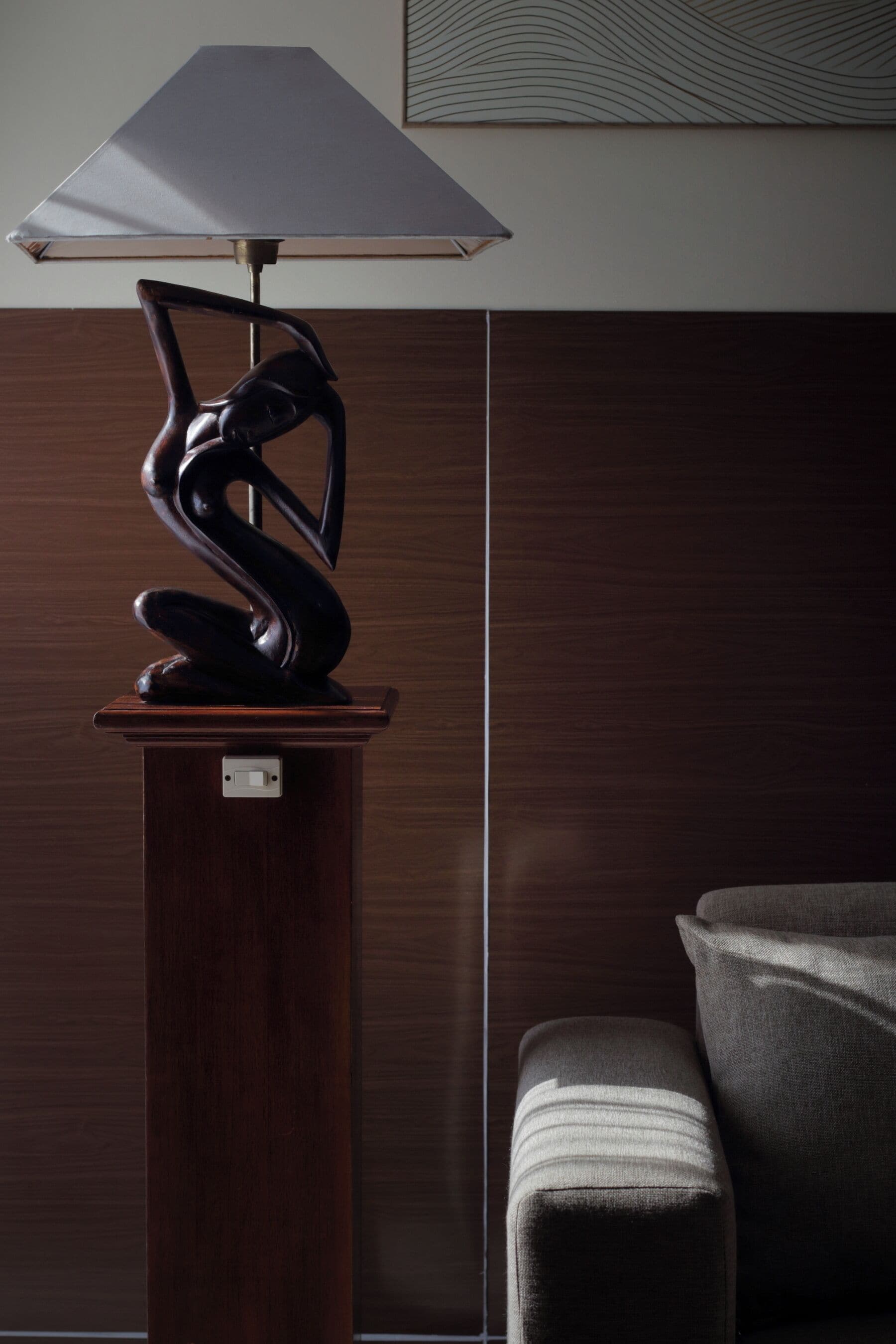 Una lámpara moderna con un diseño original sobre un pedestal de madera, una pared lisa y una esquina con un banco acolchado.