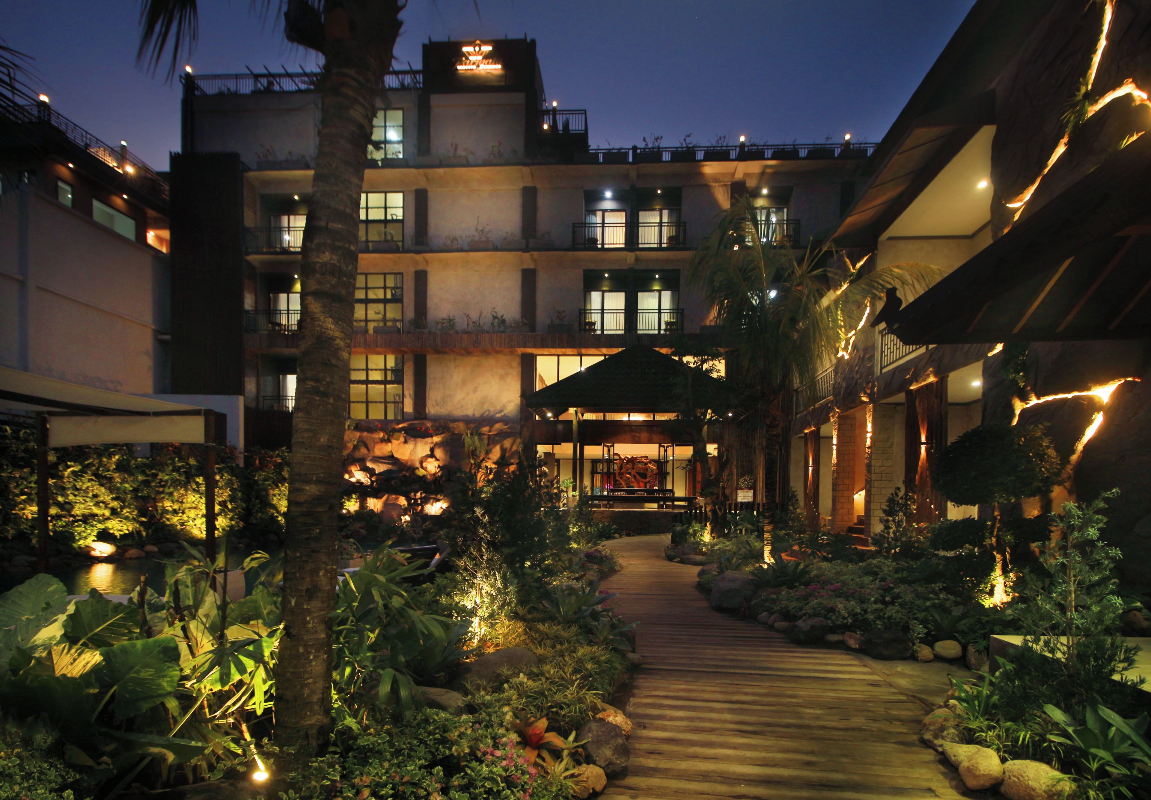 Un patio de hotel con un sendero de madera, palmeras y un jardín de rocas.