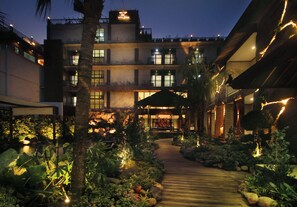 Een hotel binnenplaats met een houten pad, palmbomen en een rotstuin.