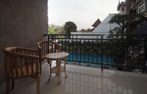 A balcony with a wooden table and chairs, overlooking a swimming pool and buildings. - Parigata Resorts Jimbaran (Jimbaran)