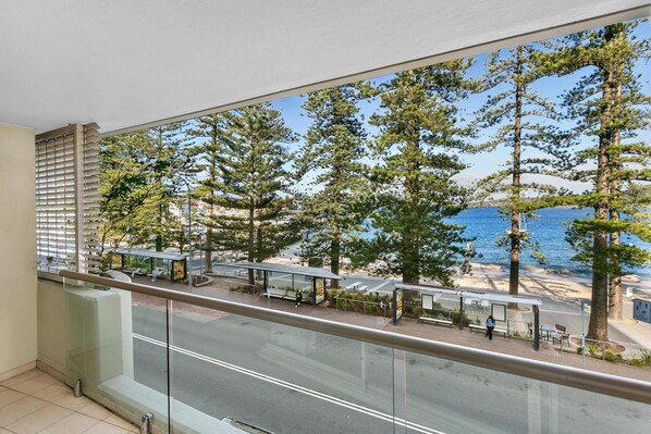 A balcony with a view of a coastal area, including trees, benches, and a bus stop.