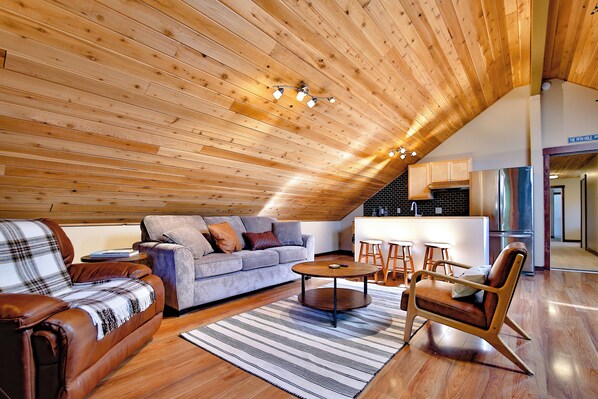 A spacious living area with a high wooden ceiling, a sofa, a coffee table, and a leather chair. - Caddy Shack Chateau- Spacious 4 bd/3.5b+Game Room, only 6 miles to Bandon Dunes! (Bandon)