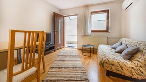 A small, well-lit room with a wooden chair, a sofa, a television, and a window with curtains. - 1 bedroom gorgeous apartment in Dekani (Dekani)