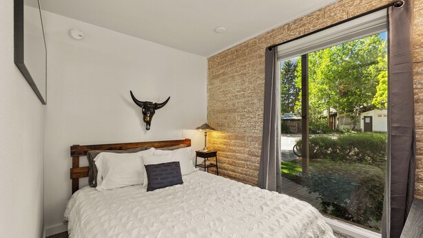 Ein Schlafzimmer mit einem großen Bett, einem hölzernen Kopfteil, einer Stierkopf-Dekoration, einem Nachttisch mit Lampe und Blick ins Grüne durch ein Fenster.