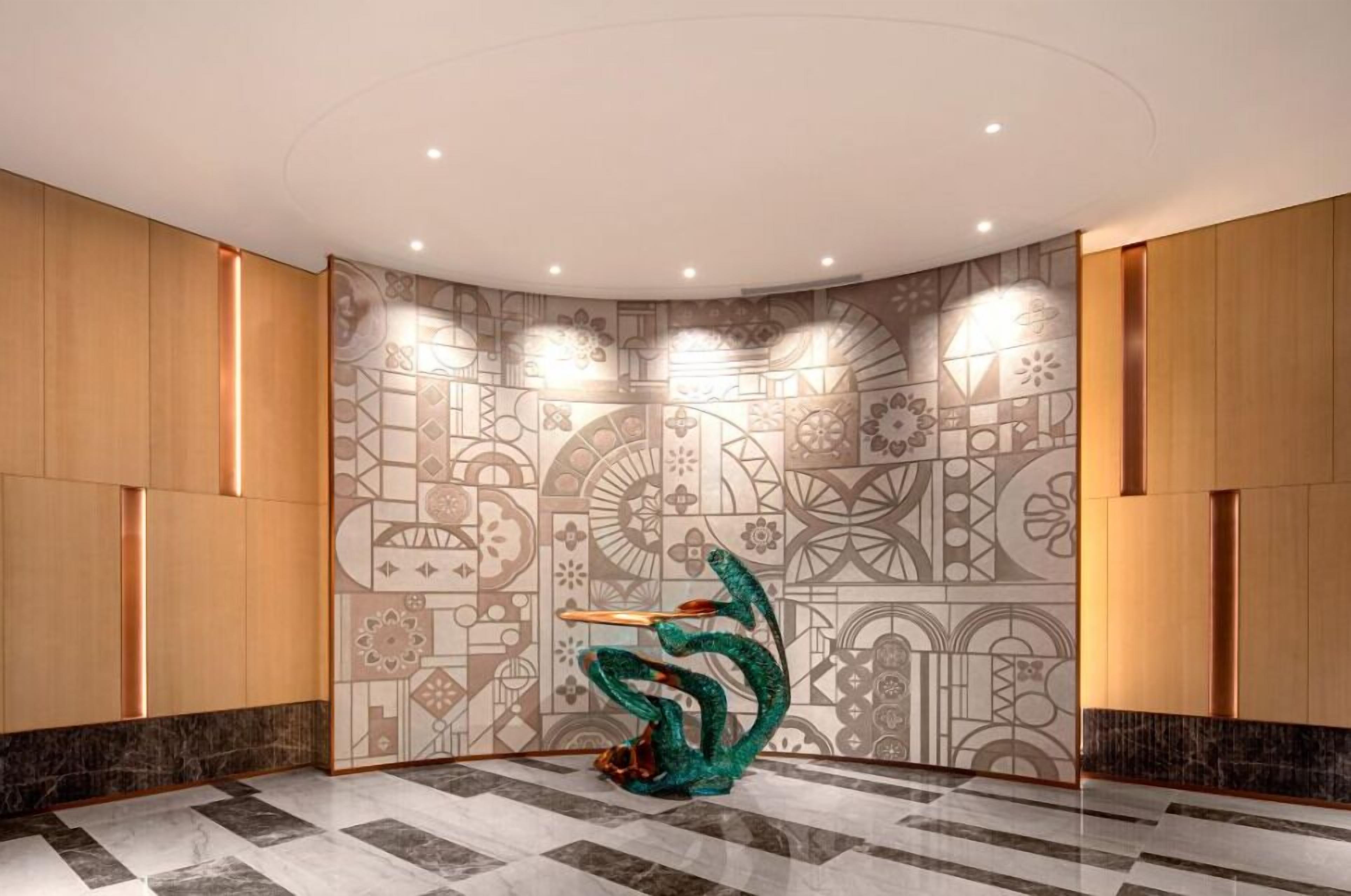 A lobby with patterned walls, a green abstract sculpture, and a polished marble floor.