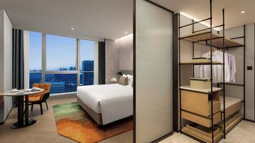 A modern hotel room with a large bed, a desk, and a view of the cityscape.