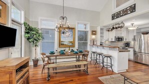 A modern kitchen with a central island, bar stools, and a dining table set for six.