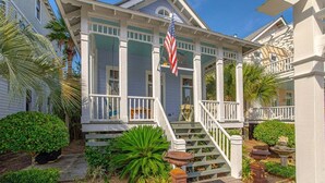 A coastal house with a porch, a flag, and a garden with plants and a birdbath.