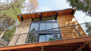 Un edificio moderno de dos pisos con fachada de madera, ventanas grandes y un balcón con barandilla de metal.