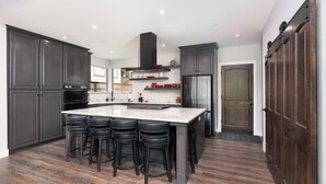 Una cocina moderna con armarios oscuros, una isla central con taburetes altos, electrodomésticos de acero inoxidable y piso de madera.