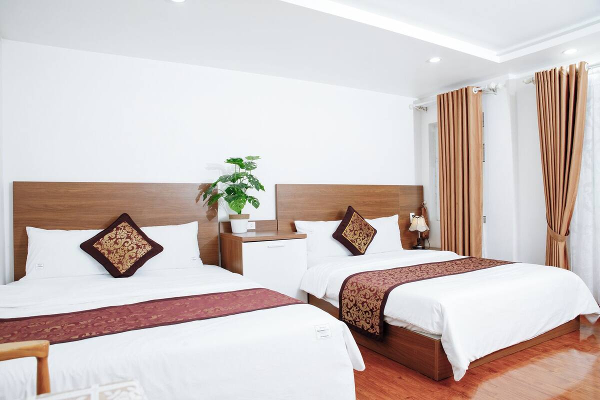 A hotel room with two beds, a nightstand, a lamp, and a potted plant.