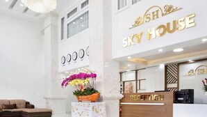 Un área de recepción con un letrero que dice "Sky House", una lámpara de araña, un mostrador de recepción y una planta con flores.