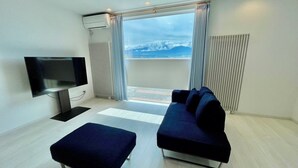 A modern living room with a flat-screen TV, a sofa, and an ottoman. - GENYA Furano (Nakafurano)