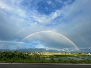 A landscape with a rainbow over a rural area with fields and distant mountains. - GENYA Furano (Nakafurano)