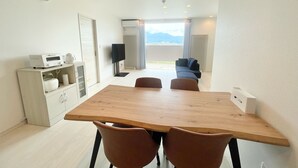 A modern room with a wooden dining table, two brown chairs, a white cabinet with a printer, a flat-screen TV, and a sofa. - GENYA Furano (Nakafurano)