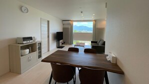 A modern room with a wooden dining table, two chairs, a sofa, a TV, and a small cabinet. - GENYA Furano (Nakafurano)